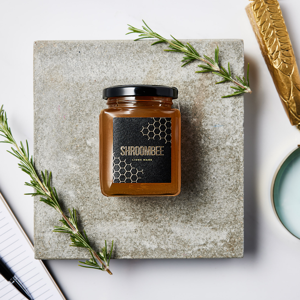 Jar of honey with a black lid on a stone surface, surrounded by rosemary sprigs.