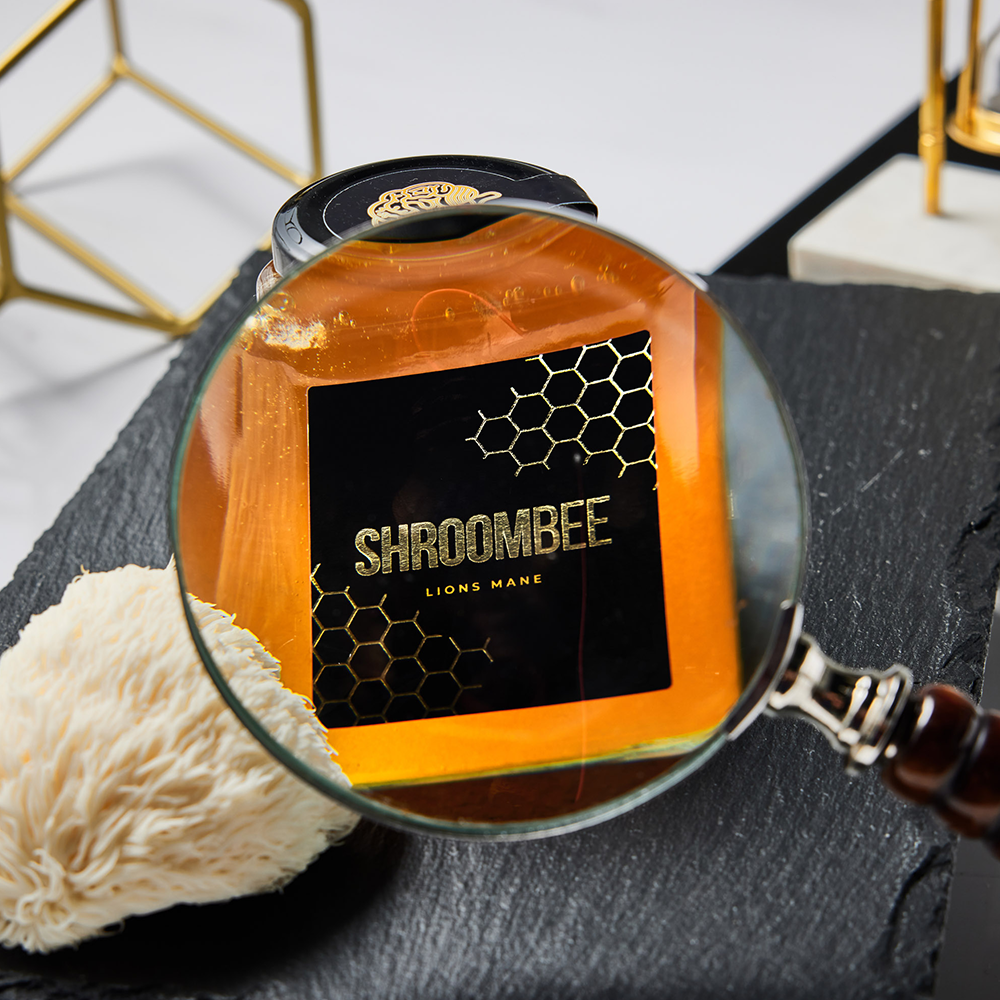Honey jar with 'Shroombee' label under a magnifying glass, with lion's mane mushroom visible.
