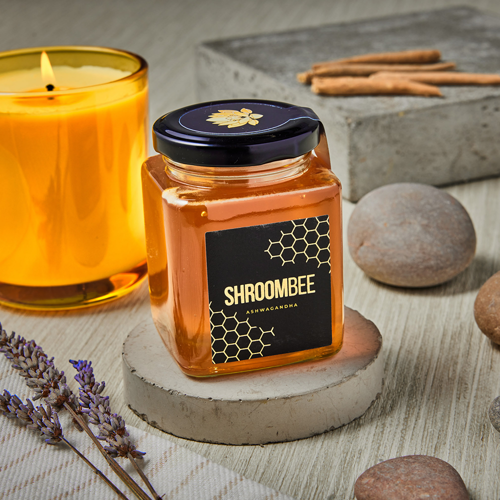 Jar of honey with 'Shroombee' label next to a lit candle on a wooden surface.