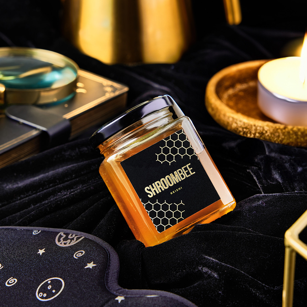 Jar of honey with 'SHROOMBEE' branding on a dark fabric background